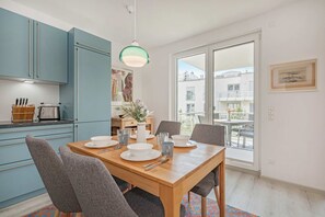 Une cuisine moderne avec des meubles bleus, une table à manger pour quatre personnes et une grande fenêtre donnant sur des immeubles.