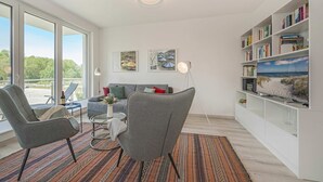 A modern living room with a sofa, armchairs, a coffee table, a bookshelf, and a TV. - Ferienwohnung Haffblick 1 - Ferienapartment in Ruhiger Lage für 2 Personen, mit Terrasse (Zirchow)