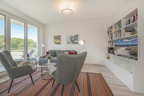 A modern living room with a sofa, armchairs, a coffee table, a bookshelf, and a TV.