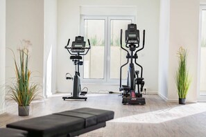 A home gym with two stationary bikes, a treadmill, and a bench.