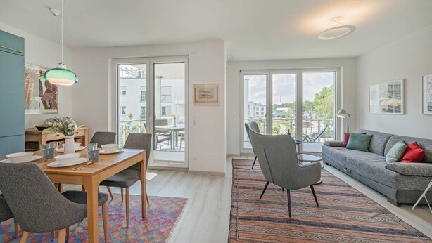 A modern apartment with a dining area, a sofa, and large windows. - Ferienwohnung Haffblick 1 - Ferienapartment in Ruhiger Lage für 2 Personen, mit Terrasse (Zirchow)