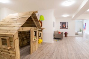 Une maison de jeu avec une cloche, un canapé gris et une petite table avec des livres.