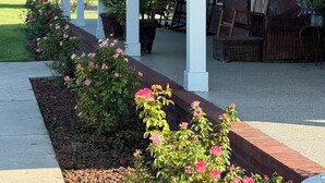 Eine Veranda mit weißen Säulen, hängenden Laternen und Gartenmöbeln.