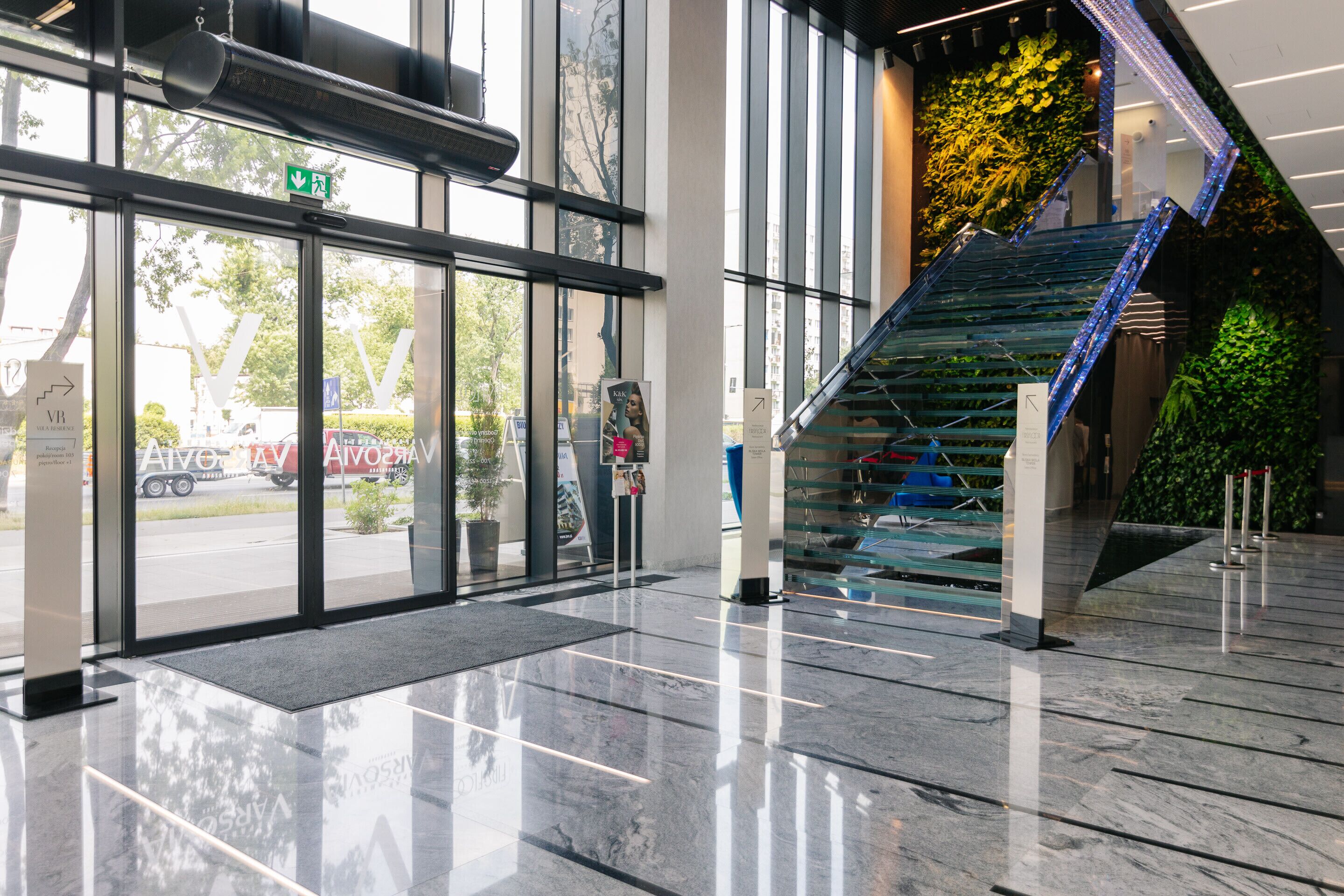 Une entrée moderne avec une porte en verre, un escalier illuminé de diodes électroluminescentes bleues et un mur végétal.