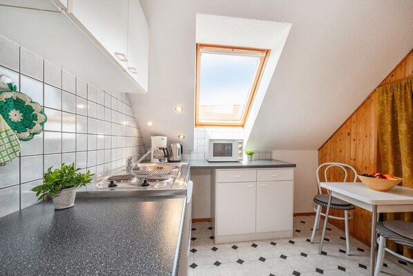 Cocina compacta con estufa a gas, microondas y un pequeño comedor con mesa y sillas.