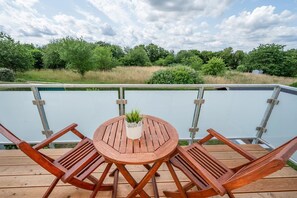 Terraza de madera con una mesa redonda y dos sillas, con vista a una piscina.