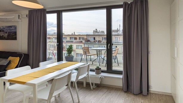 A modern living room with a dining area, large windows, and a view of the cityscape. - Cozy Apartment with Big Terrace - Karlín (Prague)