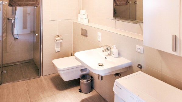 A modern bathroom with a glass shower enclosure, a white sink with a mirror above it, and a toilet.