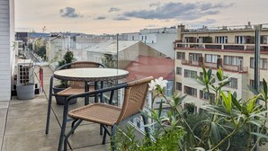 A balcony with a round table and wicker chairs, overlooking a cityscape with buildings and a cloudy sky. - Cozy Apartment with Big Terrace - Karlín (Prague)