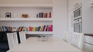 Et moderne køkken med hvide skabe, indbygget ovn og et spiseområde med et hvidt bord og stole.