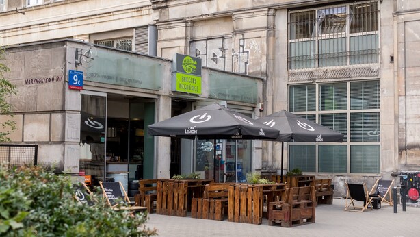 An outdoor seating area with wooden tables and chairs, a Burger's Dine-in sign, and a '100% vegan' sign.