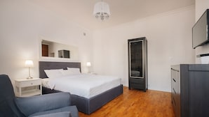 A modern hotel room with a large bed, a desk, a chair, a wardrobe, and a television.