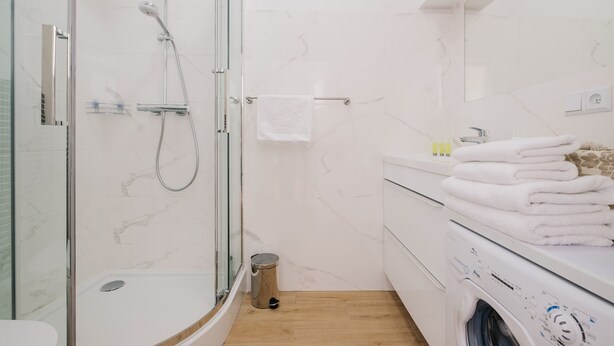 A modern bathroom with a glass shower enclosure, a built-in washing machine, and a wooden floor.