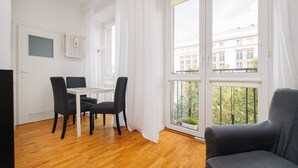 A modern room with a wooden floor, a dining table with chairs, a sofa, and large windows with white curtains.
