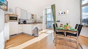 Een moderne keuken met witte kasten, een inbouwoven en een eethoek met een groene tafel en zwarte stoelen.