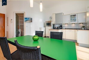 Une cuisine moderne avec des meubles blancs, une table à manger verte et des chaises en osier noires.