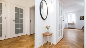 A hallway with wooden flooring, white walls, and a small table with a vase of flowers. - Royal Route Apartment for 10 people (Warszawa)