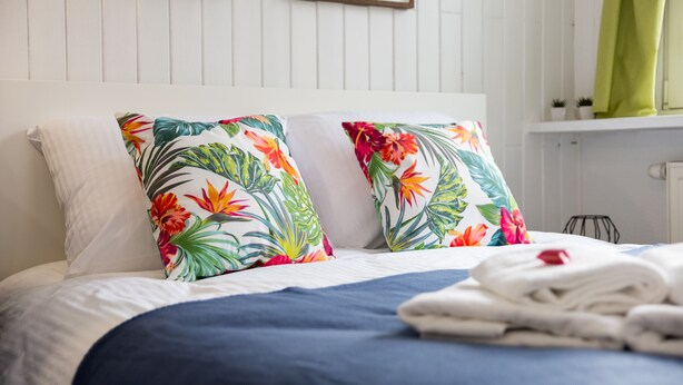 A neatly made bed with a floral pillow and a folded towel on the side. - Mokotów Cosy House Studio (Warszawa)