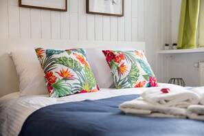 En pænt redt seng med en blomstret pude og et sammenfoldet håndklæde på siden.