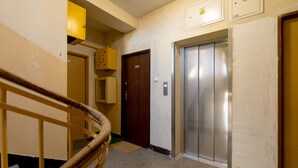 Un couloir avec une rambarde en bois, une porte et un ascenseur.