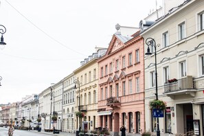 Een straat met historische gebouwen, waaronder een roze gebouw met een balkon en een bord waarop 'Hotel' staat.