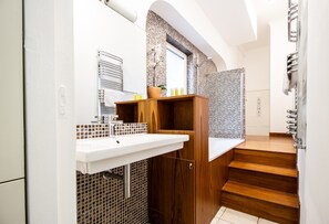 Een moderne badkamer met een houten wastafelmeubel, een witte wastafel en een betegelde douchehoek.