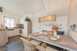 A modern kitchen with white cabinets, a built-in oven, and a dining area with a wooden table and wicker chairs.
