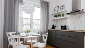 Una cocina moderna con comedor, que presenta una mesa redonda con sillas blancas, cortinas grises y vistas a edificios.