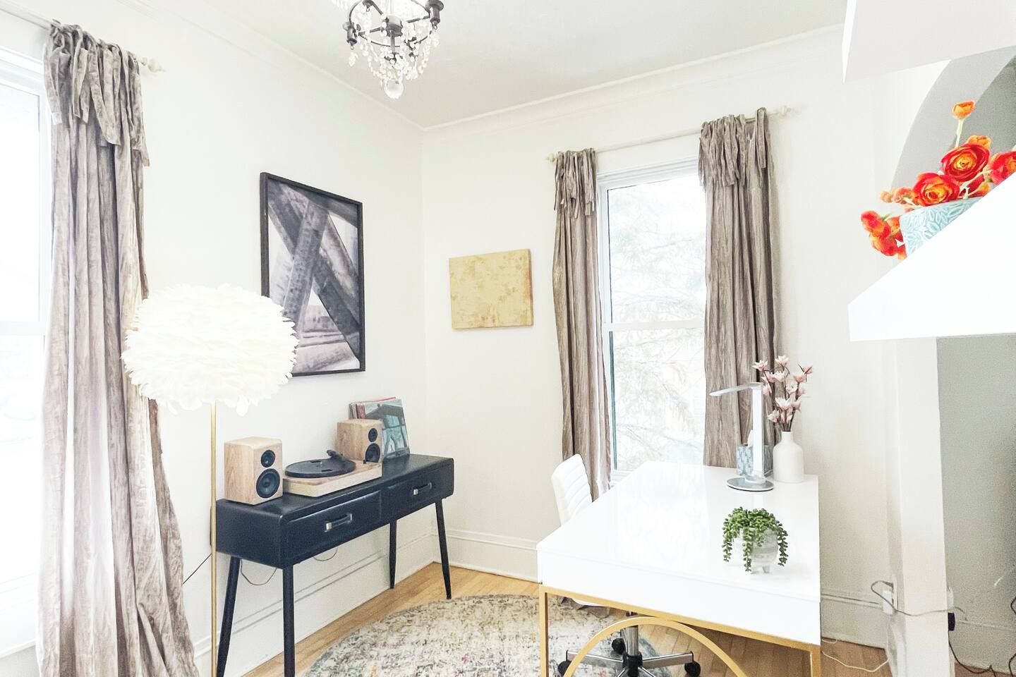 A modern room with a white desk, a black chair, a white lamp, and a chandelier.