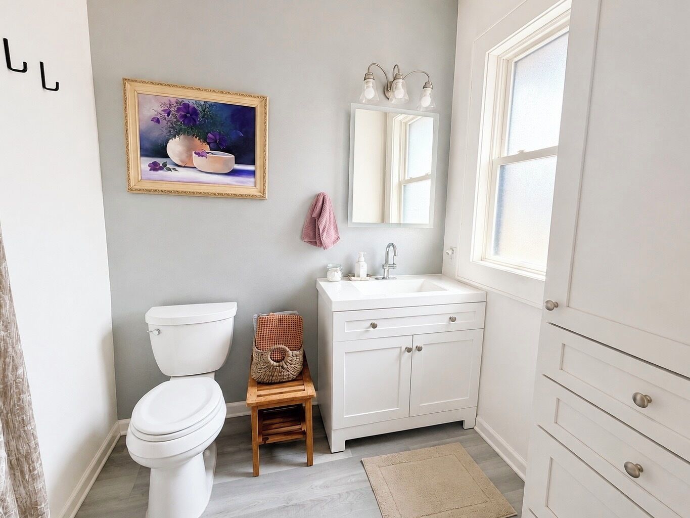A bathroom with a toilet, sink, cabinet, and a framed painting on the wall.