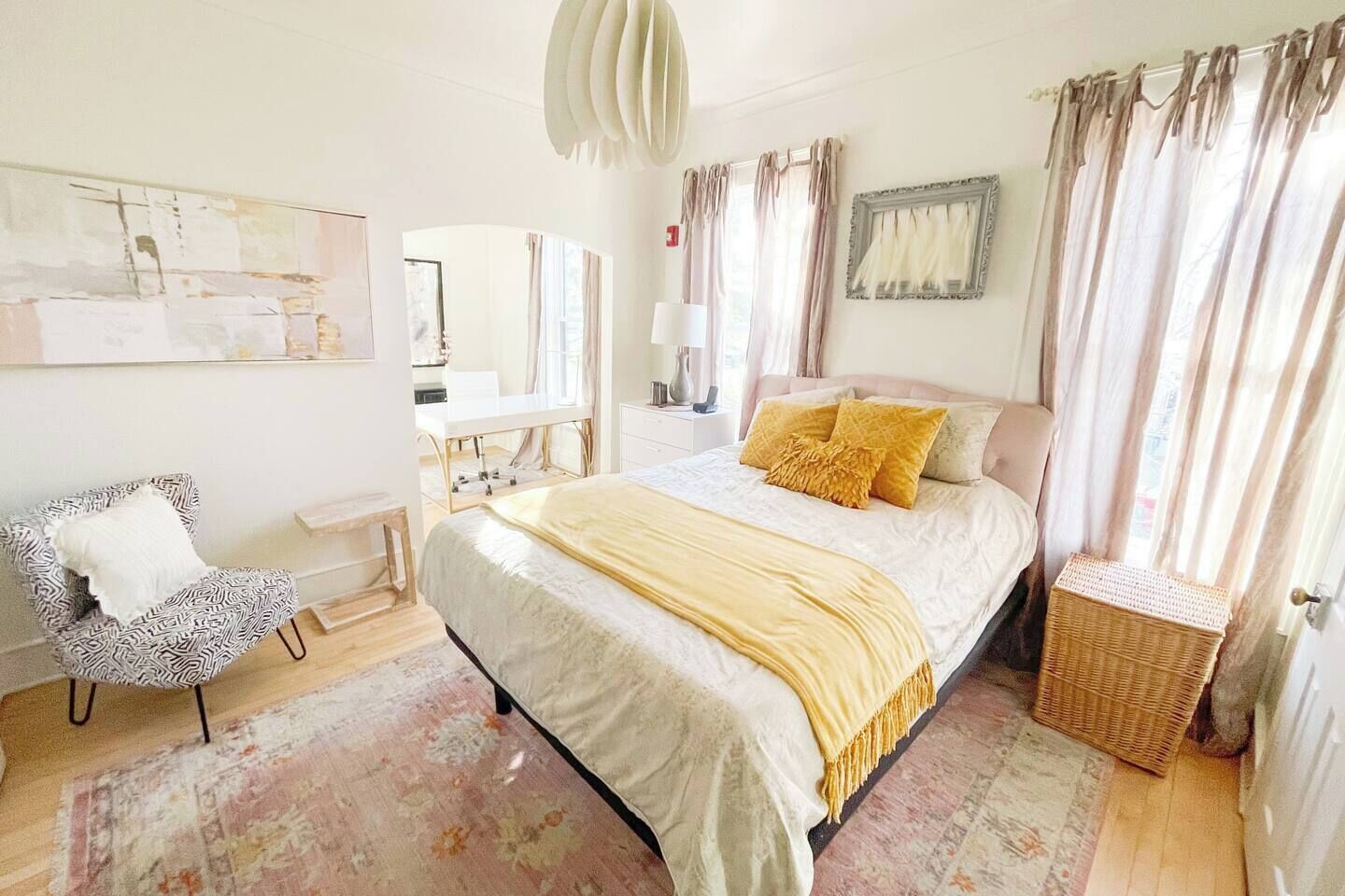 A bedroom with a bed, a chair, a bedside table, a lamp, and a window with curtains.