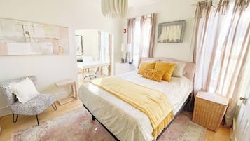 A bedroom with a bed, a chair, a bedside table, a lamp, and a window with curtains.