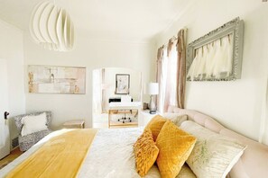 Ein Hotelzimmer mit einem großen Bett, einem Schreibtisch, einem Stuhl und Kunstwerken an den Wänden.