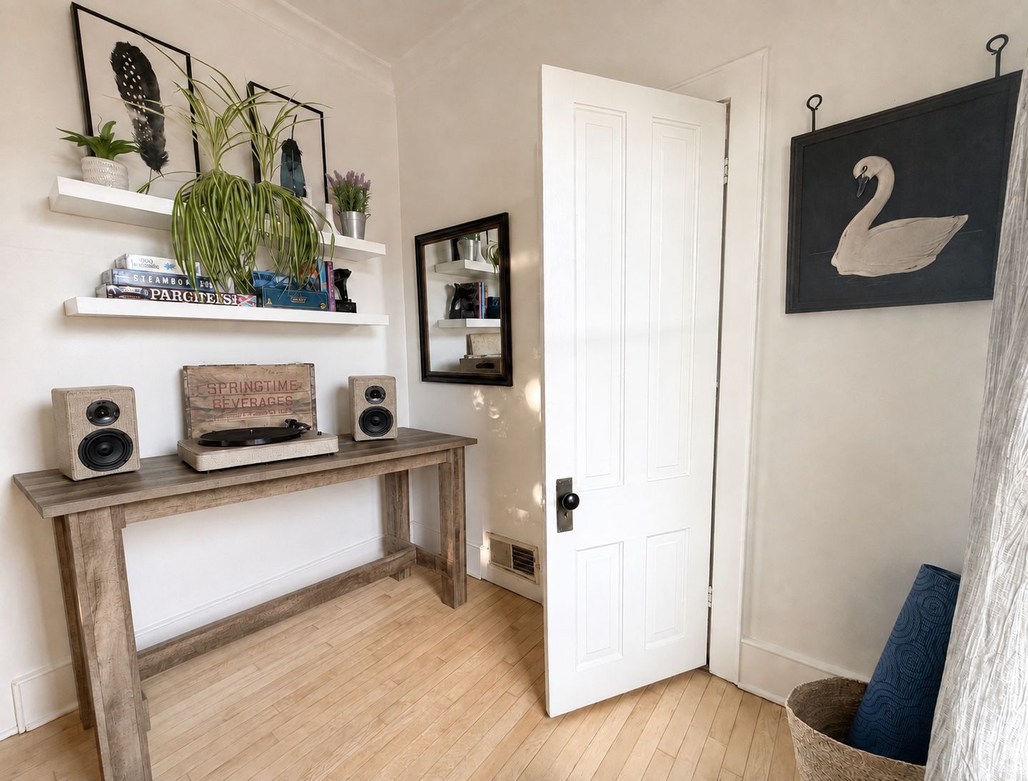 A room with a wooden console table, a white door, a wall-mounted mirror, and a framed swan picture.