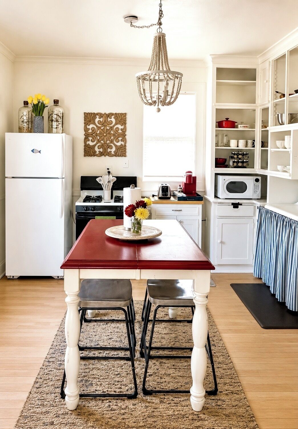 Une cuisine avec une table rouge, des placards blancs et un lustre.