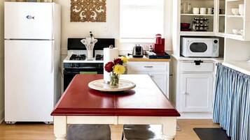 Une cuisine avec une table rouge, des placards blancs et un lustre.