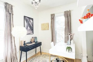 Een moderne kamer met een wit bureau, een zwarte stoel, een witte lamp en een kroonluchter.