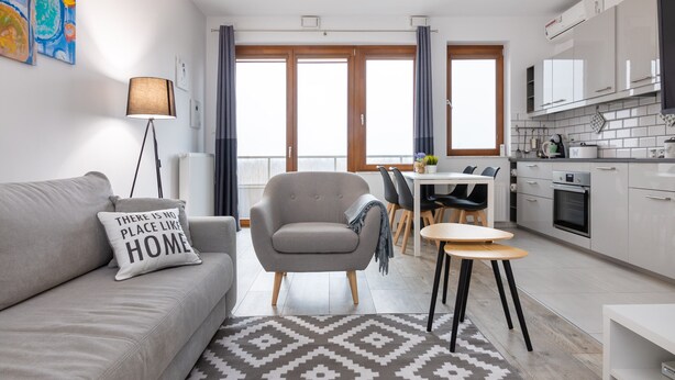 Een moderne woonkamer met een bank, een fauteuil, een eettafel met stoelen en een keuken met kasten en apparatuur.