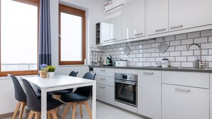 Een moderne keuken met witte kasten, een ingebouwde oven en een eethoek met een witte tafel en zwarte stoelen.