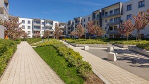 Een modern wooncomplex met een verhard voetpad, groen beplante delen en meerhoogbouwwoningen met balkons.