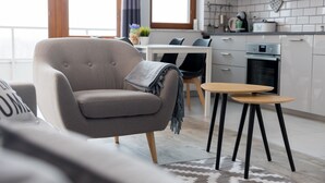 Een moderne woonkamer met een bank, een klein tafeltje, en een keukenhoek met kasten en apparatuur.