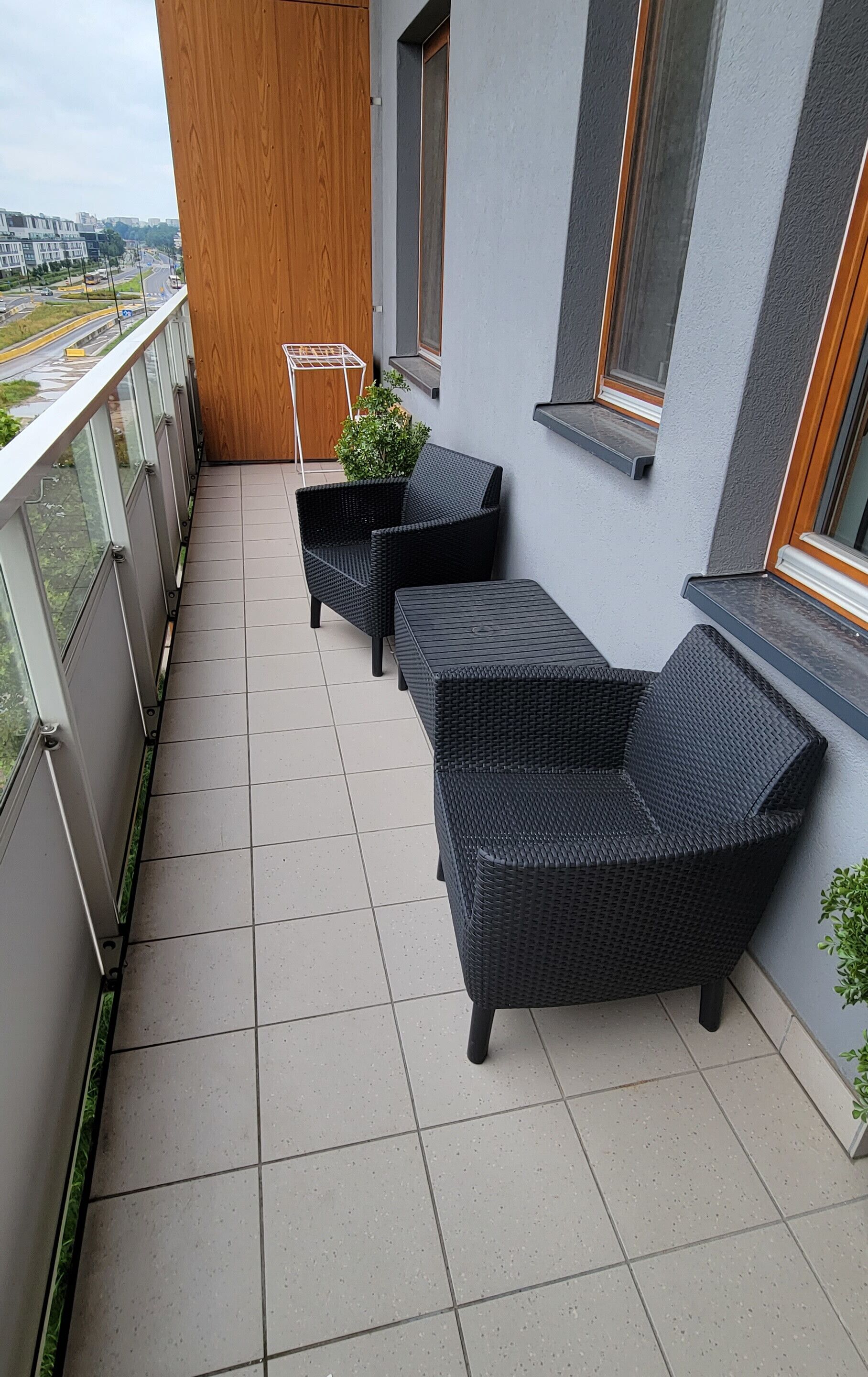 En balkon med to sorte fletsofaer, en lille potteplante og en metalkasse.