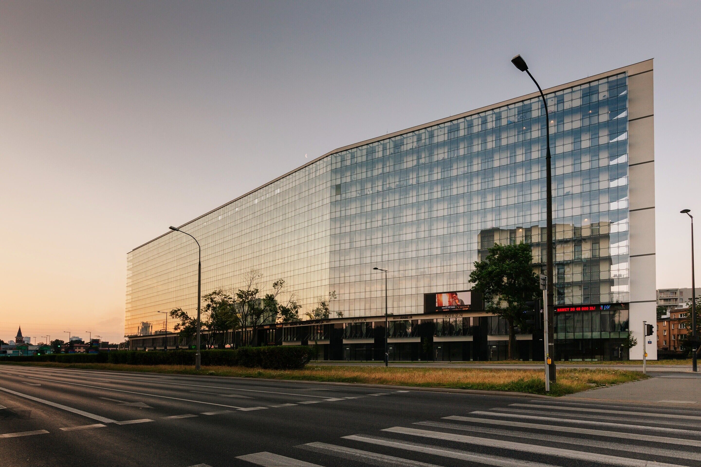 Un bâtiment moderne avec une façade en verre, un passage piéton devant et un lampadaire à proximité.