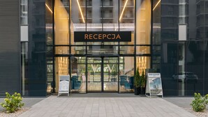 Una entrada moderna de edificio con área de recepción, puertas de vidrio y señalización.