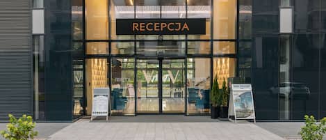 Una entrada moderna de edificio con área de recepción, puertas de vidrio y señalización.