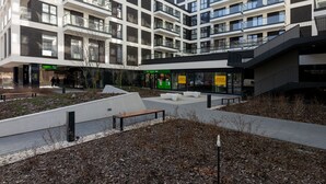 A modern multi-story building with balconies, a central courtyard, and a variety of shops at ground level.