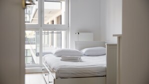 A bedroom with a bed, white bedding, and a window with a view of buildings.