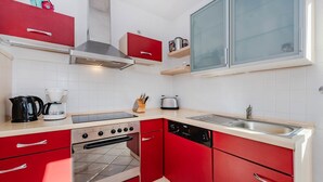 Une cuisine compacte avec des meubles de rangement rouges, une cuisinière à gaz, un lave-vaisselle et une fenêtre au-dessus de l’évier.