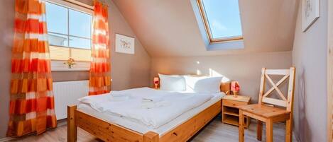 Un dormitorio con cama de madera, mesita de noche, una silla, una ventana con cortinas y un tragaluz.