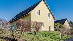 Une maison à deux étages, avec un toit en pente, un petit porche à l’avant et une pelouse bien entretenue.
